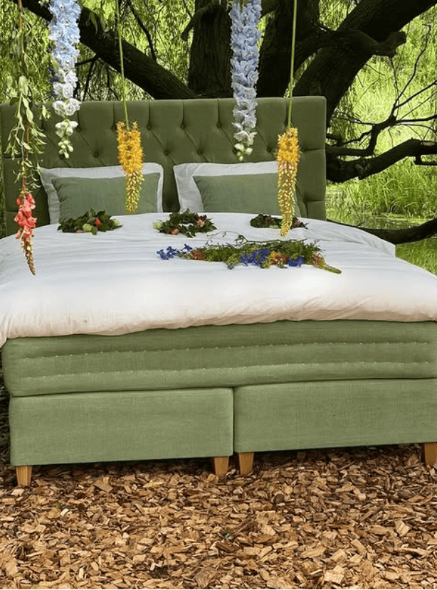 Sängfabriken - Elegant grönt sängstomme med blomsterdekoration i naturmiljö.